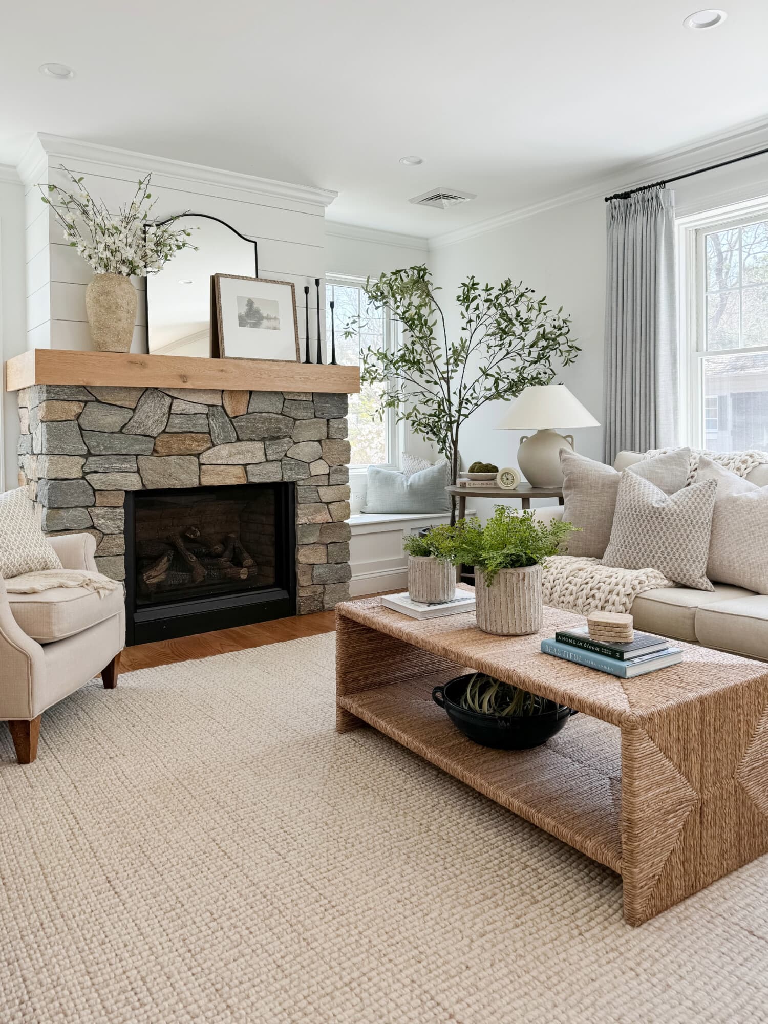 Bright living room with a stone fireplace, woven coffee table, and neutral furniture and decor.