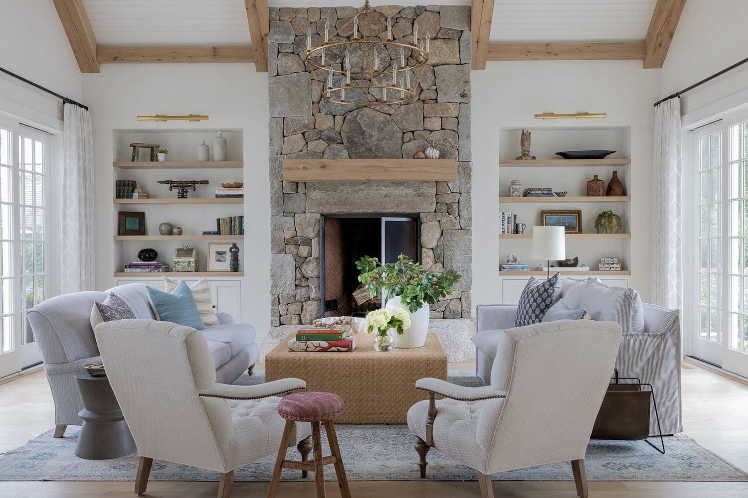 Bright living room featuring a stone fireplace, wooden beams, and comfortable white upholstered seating.