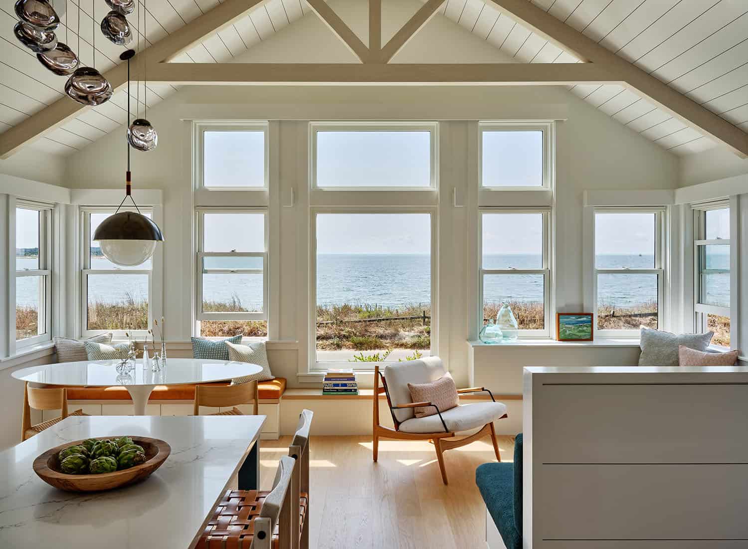 Bright coastal living area with vaulted ceilings and large windows overlooking the calm ocean.