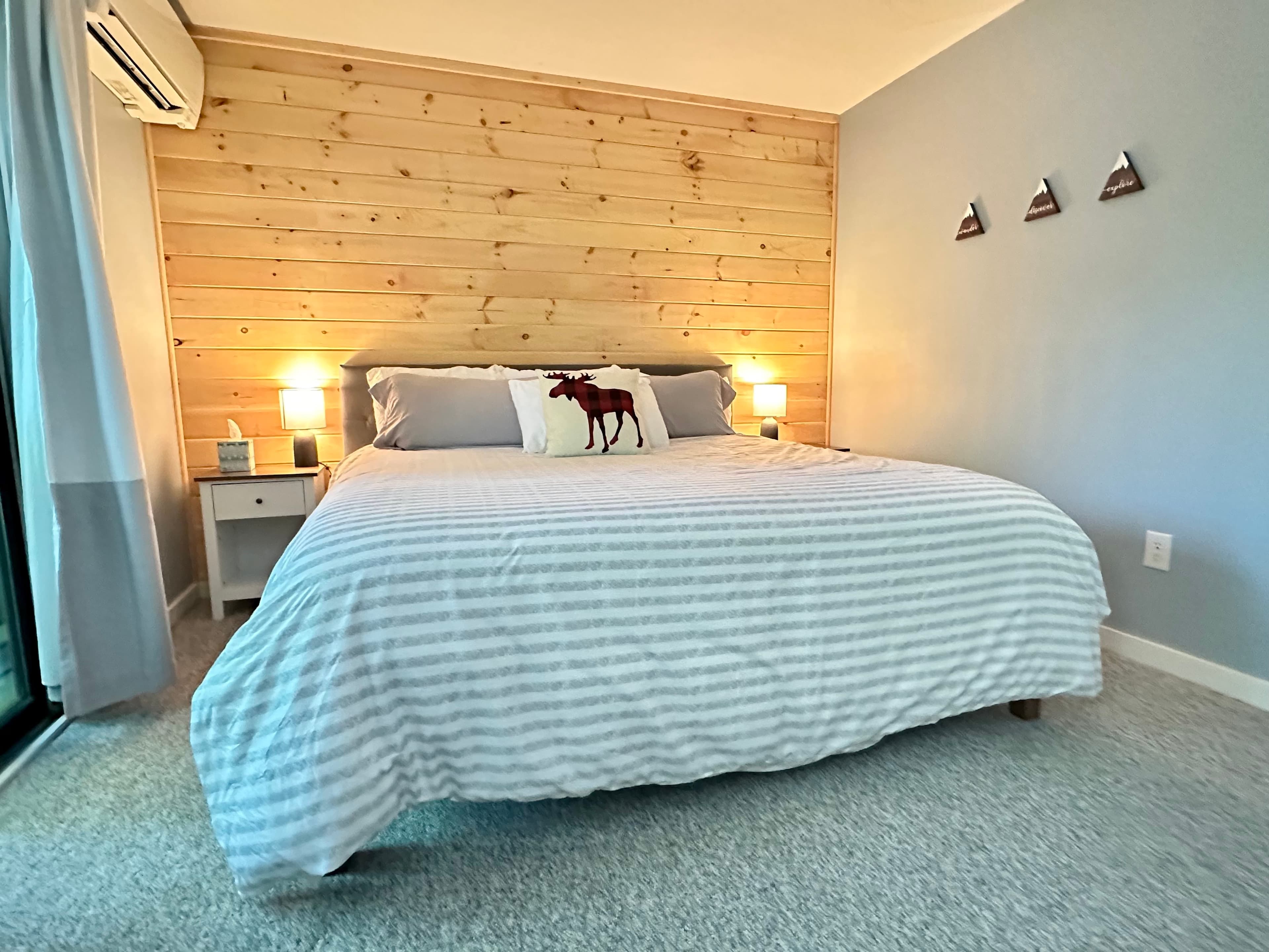 Cozy bedroom with a wood-paneled wall, striped bedding, and a red moose silhouette pillow.