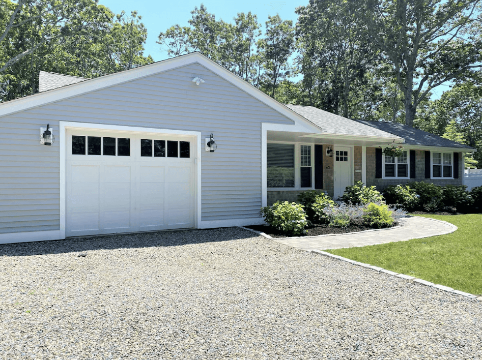 Light blue house with white garage door, gravel driveway, and curved stone walkway.
