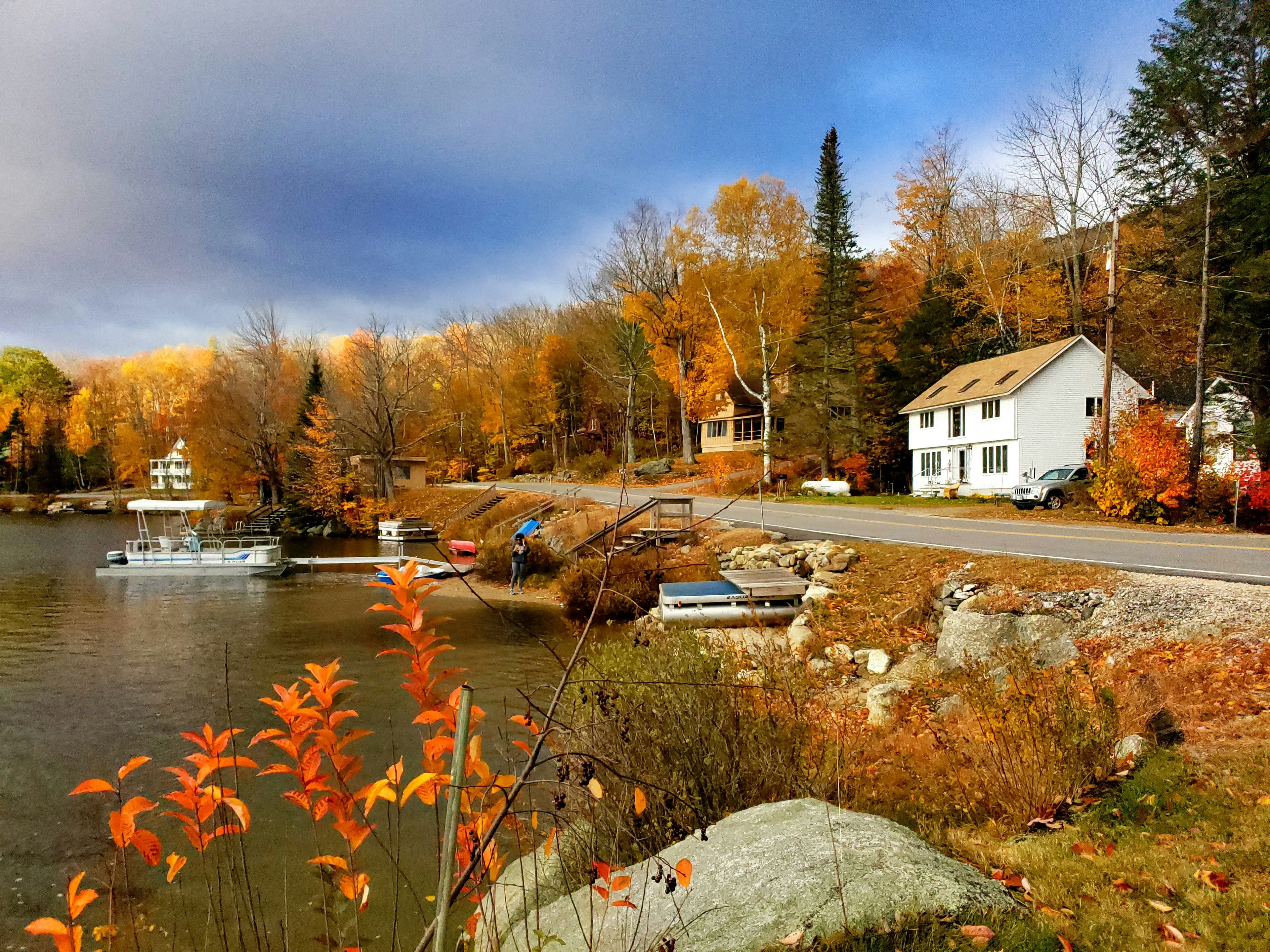 Vibrant autumn foliage surrounds a peaceful lake with a white house and docked boat.