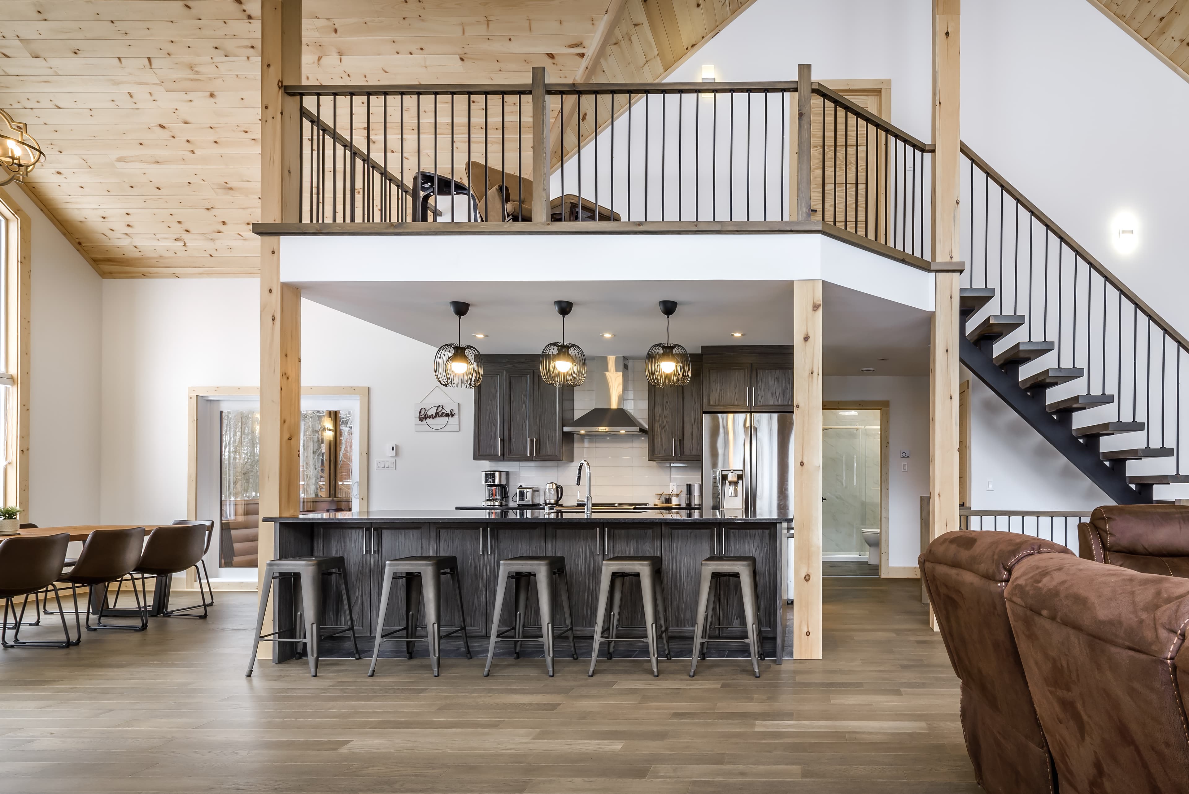 Modern rustic kitchen with dark cabinets, a large island, and a wooden mezzanine loft.